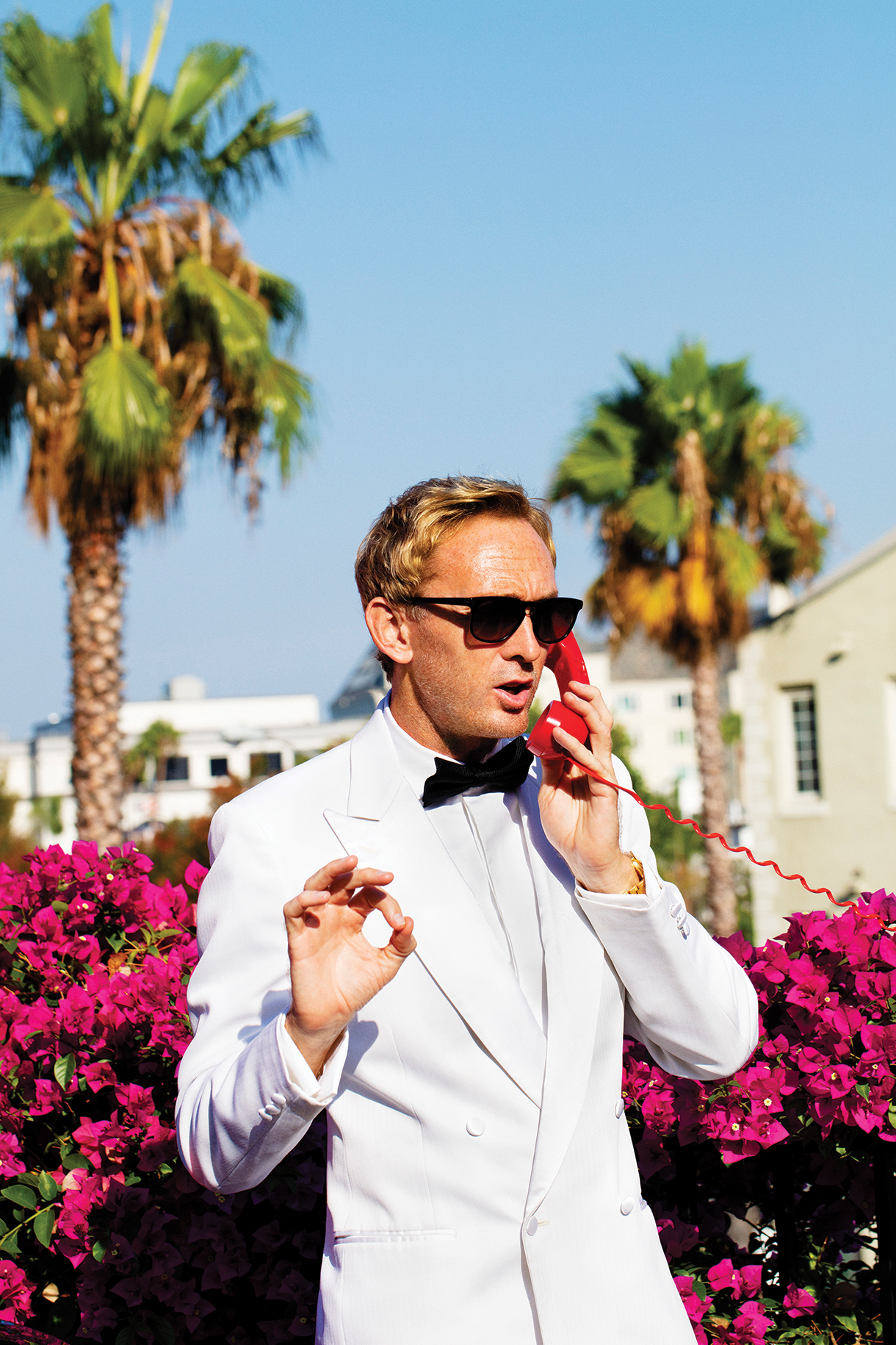 Man dressed in white tuxedo wearing black sunglasses and holding a red telephone in Hollywood, California